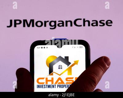 In dieser Abbildung wird das Chase Investment Property-Logo auf einem Smartphone-Bildschirm mit einem JPMorgan Chase & Co-Logo im Hintergrund angezeigt Stockfoto