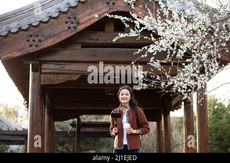 Junge Frau, die ein Selfie unter einem Pfirsichblütenbaum fotografiert - Stockfoto Stockfoto