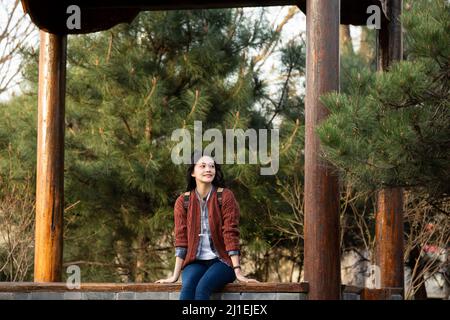 Junge chinesische Universitätsstudentin, die sich in einem Pavillon mit einem Stock-Foto entspannt Stockfoto