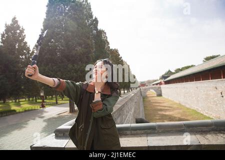 Junge weibliche Tourguide hält Selfie-Stick, um Live-Video auf Smartphone zu streamen - Stock Foto Stockfoto