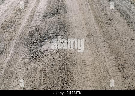 Bröckelnder Feldweg ohne Asphalt, aus Lehm und Schmutz mit Schutt, mit Gruben und Schlaglöchern gefüllt mit Wasser, Pfützen nass nach Regen Stockfoto