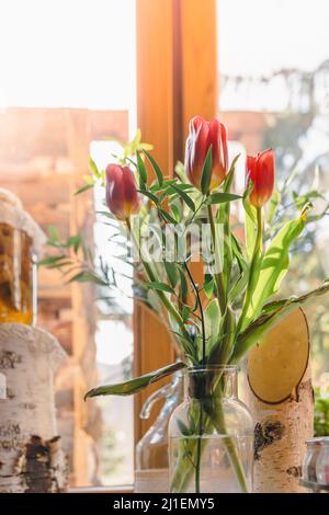 Blumenstrauß mit Frühlingsblumen Tulpen in Vase auf Fensterbank in Sonnenstrahlen Stockfoto