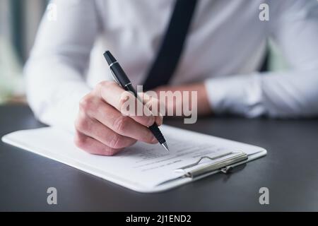 Alle richtigen Kästchen ankreuzen. Eine ausgeschnittene Aufnahme eines Geschäftsmanns, der Papierkram auf einem Klemmbrett ausfüllt, während er an einem Tisch in einem Büro sitzt. Stockfoto