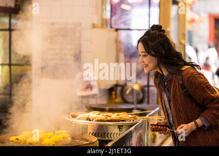 Junge chinesische College-Student Auswahl gedämpfter Reis Kuchen in einer Lebensmittelstraße in Peking - Stock Foto Stockfoto