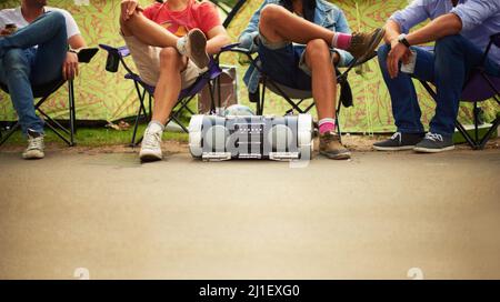 Chillen im Takt. Vier Freunde genießen Musik von einer Stereoanlage, während sie auf Campingstühlen bei einem Musikfest sitzen. Stockfoto