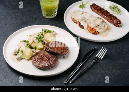 Kartoffelpüree mit Patties auf pflanzlicher Basis und vegetarische Gemüsespieße mit Süßkartoffeln, Sahnesauce und Parmesan. Dunkler Betonhintergrund Stockfoto