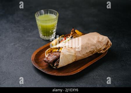 Fleisch-Kebab auf pflanzlicher Basis in Lavasch auf einem Holzteller mit gegrilltem Gemüse und Saft auf dunklem Beton-Hintergrund. Platz kopieren Stockfoto