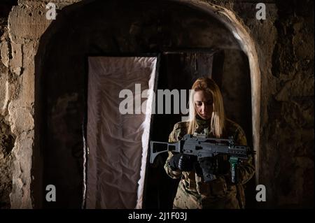 Kaukasische Frau in Armeeuniform, die ein Maschinengewehr hält und in der Nähe eines offenen Sarges steht. Stockfoto