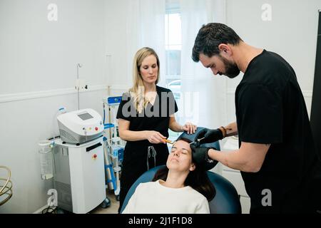 Eine Frau, die von einem Arzt und einer Krankenschwester Botulinumtoxin oder Füllstoffe auf Stirn und Gesicht bekommt Stockfoto
