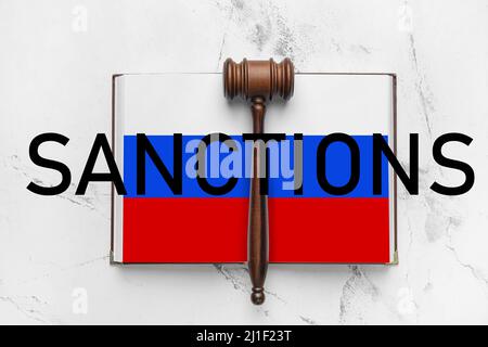 Offenes Buch mit Seiten in den Farben der russischen Flagge, Richtergavel und WORTSANKTIONEN auf hellem Hintergrund Stockfoto