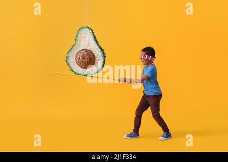 Kleiner Junge bricht mexikanische Pinata auf farbigem Hintergrund Stockfoto