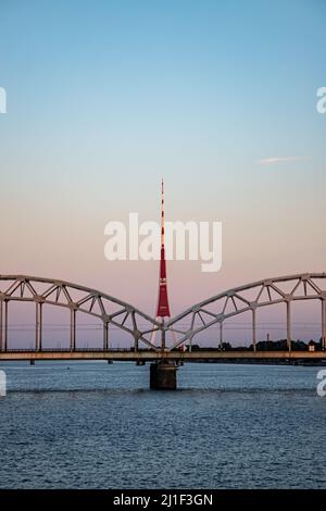 Riga, Lettland - 15.08.2021 Blick auf den Radio- und Fernsehturm von Riga und die Eisenbahnbrücke bei Sonnenuntergang Stockfoto