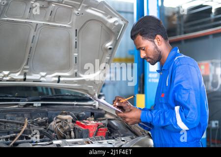 Konzentrieren Sie sich auf die Hände Auto Mechaniker notieren Reparaturteile während der offenen Motorhaube Motorreparatur in der Garage - Konzept der Kundenbericht, professionelle Arbeiter und Stockfoto