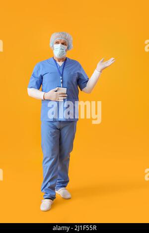 Reifer Arzt in medizinischer Maske zeigt etwas auf gelbem Hintergrund Stockfoto