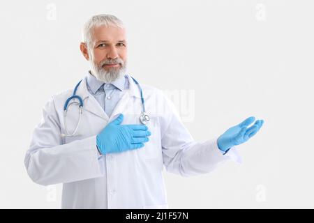Reifer männlicher Arzt mit Stethoskop, das etwas auf weißem Hintergrund zeigt Stockfoto