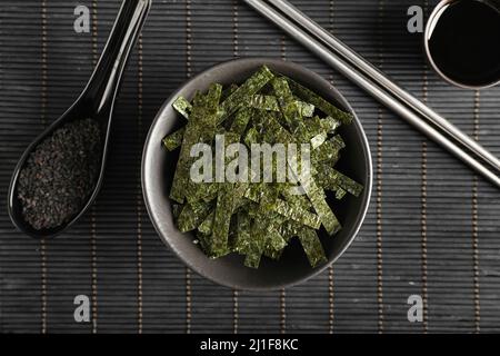 Schüssel mit gehackten Algenblättern und Löffel Sesam auf Bambusmatte Stockfoto