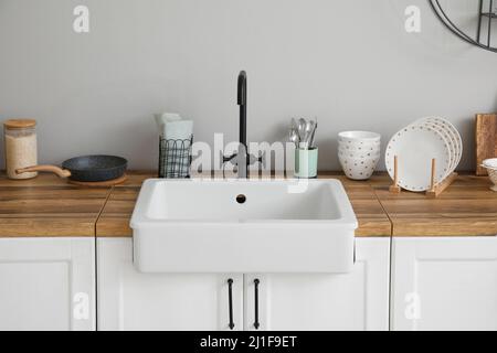 Theken mit Keramikwaschbecken, Küchenutensilien und Essen in der Nähe einer hellen Wand Stockfoto