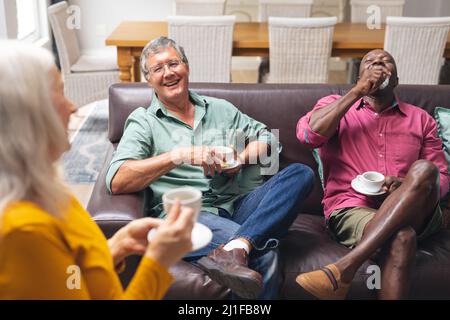 Glückliche multirassische ältere männliche und weibliche Freunde, die zu Hause Kaffee trinken Stockfoto