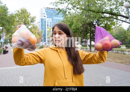 Die Frau hält Gemüse und Obst in einer Plastiktüte und einem Stoffkäufer. Stockfoto