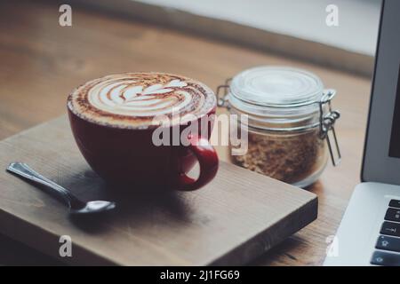 Cappuccino in einer roten Tasse und einem Glas mit Müsli Stockfoto