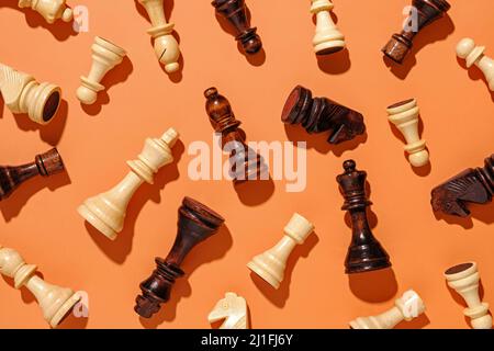 Verstreute Schachfiguren aus Holz auf einem orangefarbenen Hintergrund, die in zufälliger Reihenfolge als flaches Stillleben angeordnet sind Stockfoto