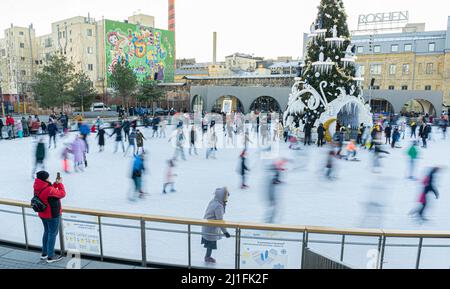 Ukraine, Kiew - 7. Januar 2022: Eislaufbahn im Winter. Die Leute laufen. Schlittschuhe fahren auf Eis. Eislaufen ist ein Wintersport-Unterhaltung. Weihnachtszeit. Weihnachtsbaum Roshen Fabrik. Menge Stockfoto