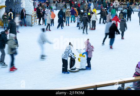 Ukraine, Kiew - 7. Januar 2022: Eislaufbahn im Winter. Die Leute laufen. Schlittschuhe fahren auf Eis. Eislaufen ist ein Wintersport-Unterhaltung. Weihnachtszeit. Weihnachtsbaum Roshen Fabrik. Menge Stockfoto