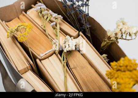 Nahaufnahme von getrockneten Blumen auf Büchern in Einkaufstasche isoliert auf grauer Ansicht von oben Stockfoto