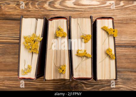 Draufsicht auf Bücher mit getrockneten gelben Blüten auf Holzoberfläche Stockfoto