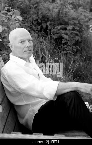 Porträt eines hübschen kahlen Mannes, der im Garten sitzt. Schwarzweiß-Foto Stockfoto