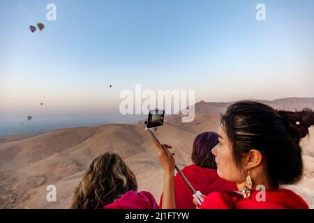 Hübsche junge Frau in Rot, die Selfies macht, während sie in einem Heißluftballon in Luxor fliegt Stockfoto