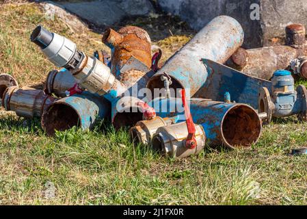 Metallschrott, Stapel von alten geschnittenen und verrosteten Rohrleitungen mit großen defekten Ventilen auf dem Rasen Stockfoto