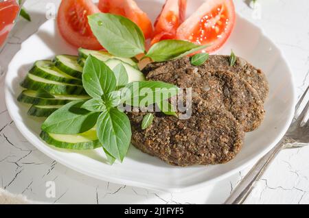 Rohes Schnitzel aus Gemüse und Getreide mit Gemüse und Kräuter auf einem weißen Teller mit hartem Licht Stockfoto