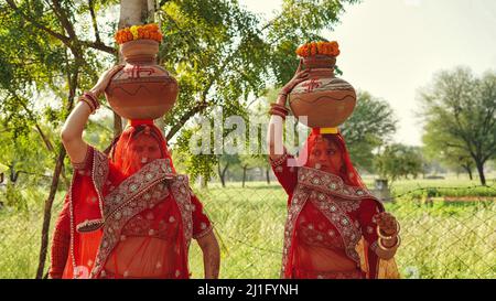 23 März 2022 Reengus, Rajasthan, Indien. Nicht identifizierte indische Neubraut in farbenfrohen traditionellen Kleidern trägt Wasser in Tontöpfen Stockfoto