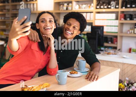 Fröhliche kaukasische Frau, die Selfie mit afroamerikanischem Freund im Café macht. Unverändert, Café-Kultur, Menschen, Liebe, Technologie und Livestyl Stockfoto