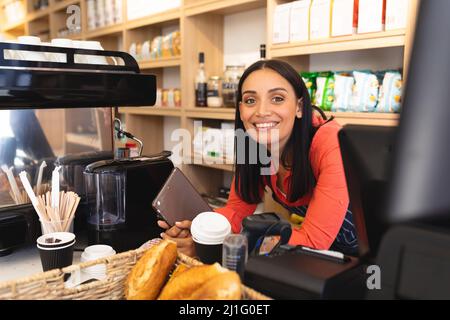 Fröhliche junge kaukasische Barista mit Tablet-pc, der sich auf der Theke im Café stützt. Unverfälscht, Café-Kultur, Menschen- und Berufskonzept. Stockfoto