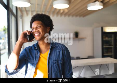 Glücklicher junger afroamerikanischer Kunde, der im Coffee Shop auf dem Smartphone spricht. Unverändert, Cafekultur, Menschen, Technologie und Lifestyle-Konzept. Stockfoto