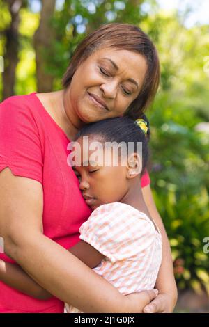 afroamerikanische ältere Frau umarmt Enkelin mit geschlossenen Augen im Hinterhof Stockfoto