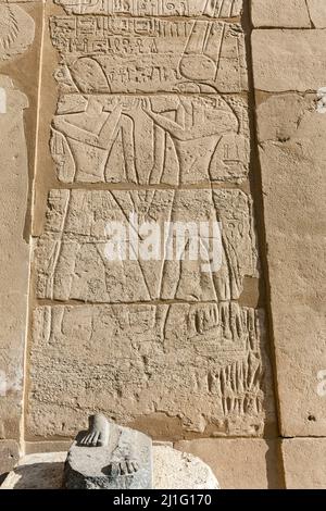 Verbliebene Füße der alten ägyptischen Statue, vermutlich Ramses II, in Karnak, mit Inschrift auf Wand hinter dem pharao und dem gott Amun Ra Stockfoto