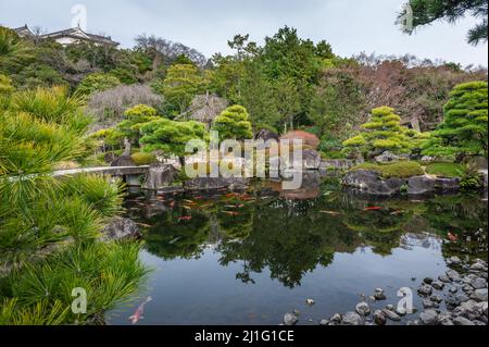 Himeji, Japan - 6. Januar 2020. Außenaufnahme eines japanischen Gartens mit einem Teich mit bunten Fischen in der Nähe des Schlosses Himeji. Himeji Schloss in einem der letzten verbliebenen authentischen Schlösser in Japan und eine beliebte Touristenattraktion. Stockfoto