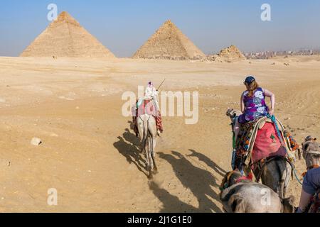 Touristen reiten auf Kamelen in der Nähe der Pyramiden von Chephren und Menkaure, Gizeh, Ägypten Stockfoto