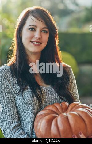 Ohne ein Lächeln kann man Kürbis nicht sagen. Porträt einer jungen Frau, die einen Kürbis draußen hält. Stockfoto