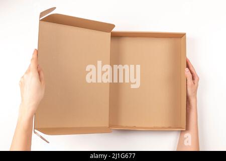 Draufsicht auf weibliche Hände, die einen leeren braunen Karton auf weißem Hintergrund öffnen. Nachbau-Paketkasten. Verpackung, Einkauf, Lieferkonzept Stockfoto