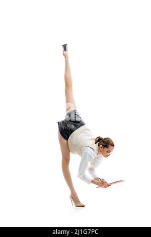 Dynamisches Porträt einer jungen flexiblen Frau, Büroangestellter in stilvollen Stofflesepapieren, isoliert im Garn über weißem Studiohintergrund stehend Stockfoto