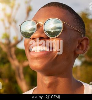 Nun, das nenne ich eine Aussicht. Aufnahme eines glücklichen jungen Mannes, der eine Sonnenbrille trägt, während er die Aussicht von draußen bewundert. Stockfoto