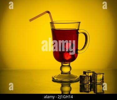 Kalter Tee, Cocktail, Fruchtgetränk in einer hohen Glasschale mit Trinkhalm auf einem Tisch mit Eisstücken. Rotes Getränk mit Eis in einem Becher auf einem schönen Br Stockfoto