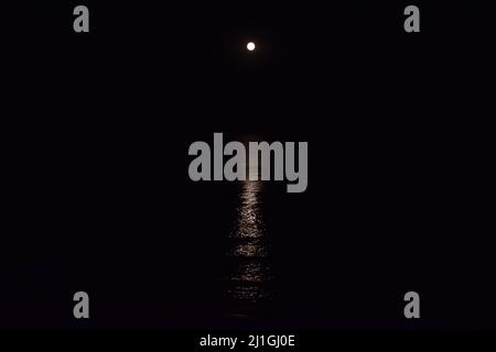 Der Vollmond am Strand. Die Mondbahn spiegelt sich im Wasser wider. Der Nachtmond kam über dem Wasser auf. Vollmond am Strand. Vollmond in der Nähe Stockfoto