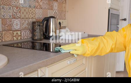 Ein Mann in Schutzkleidung reinigt und führt in der Küche in der Wohnung eine sanitäre Reinigung durch. Stockfoto