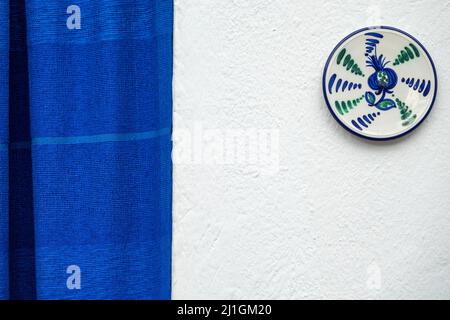 Eingang eines ländlichen andalusischen Hauses mit einem blauen Vorhang und einer typischen Keramikplatte an der weißen Fassade Stockfoto