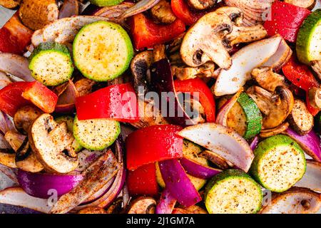 Nahaufnahme Ansicht von rohem Gemüse gewürzt mit Olivenöl und Gewürzen: Ansicht von oben aufgeschnittenem und gewürztem Gemüse auf einer Blechpfanne Stockfoto